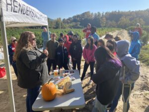 Students inspect a pumpkin under a tent.