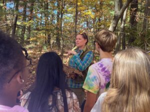 Students listen to an adult in a forest.