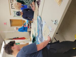 A group of kids take instruction on sewing from adults.