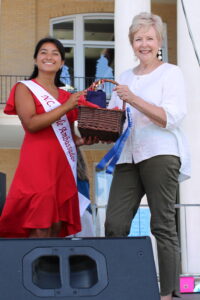 Woman on the left handing gift basket to woman on the right. 