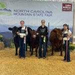 competitors posing with cows in front of mountain state fair backdrop
