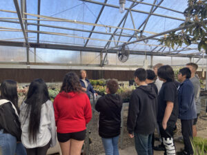 Students listen to a lecture in a green house.