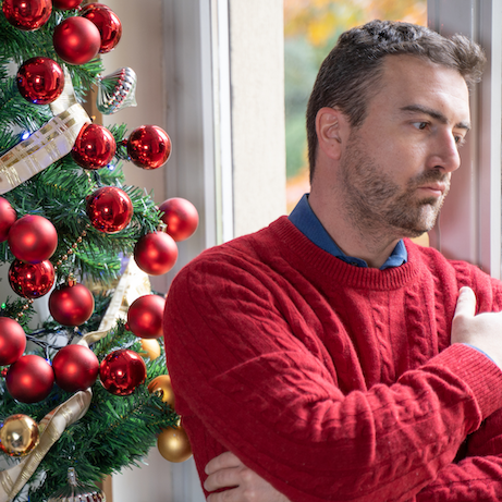 Man deep in thought standing by Christmas tree