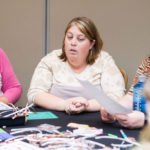 Women sit together at a table reading instructions.