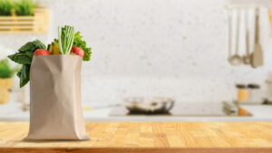 A brown paper grocery bag filled with fresh produce on a kitchen countertop.