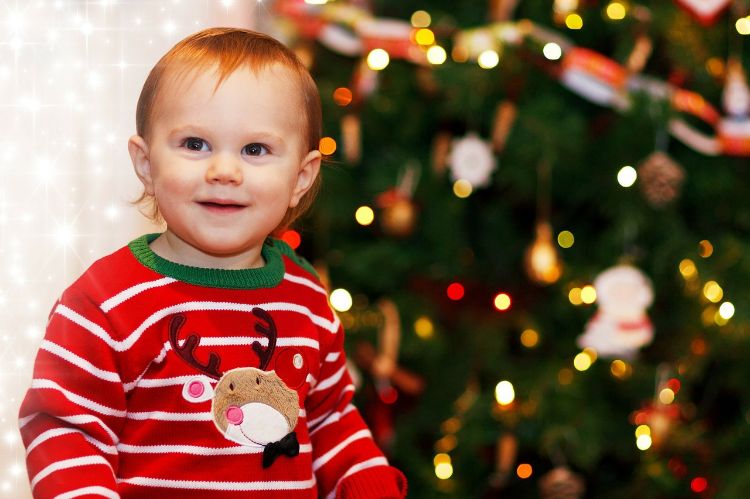 A toddler sits in front of a Christmas tree.